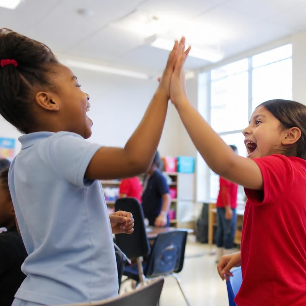 Two students high-fiving across a classroom table