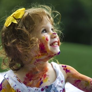 A little girl with paint on her cheeks smiling up at something out of frame