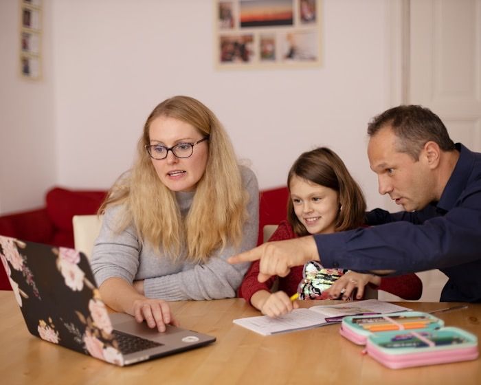 Two parents and their daughter looking at a laptop together at the dining table