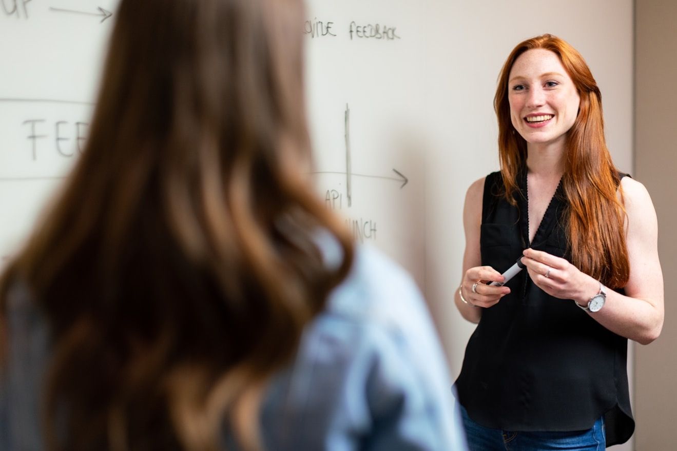 A teacher smiling as she explains something to a student at the whiteboard