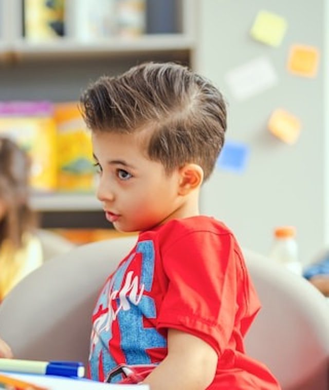 A boy in a classroom, listening attentively with his hand raised