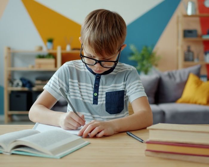 A boy concentrating as he writes at a desk with books open in front of him